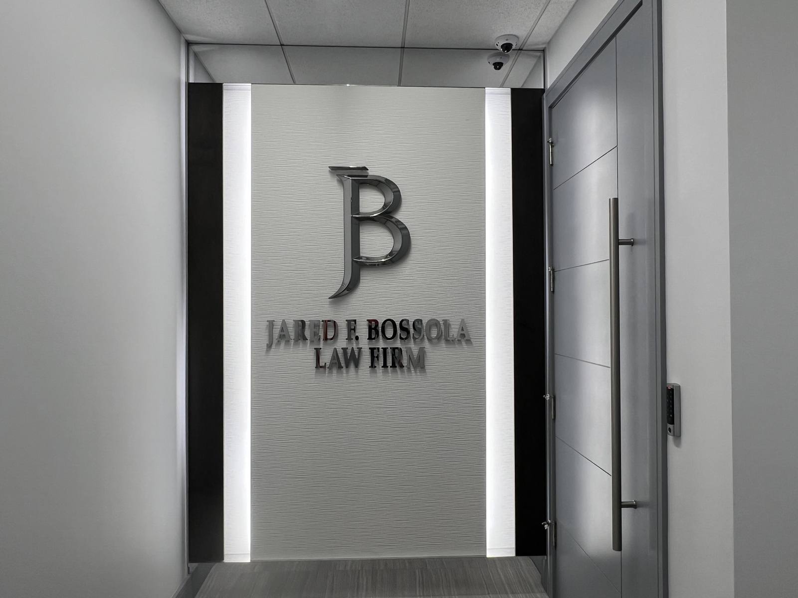The entrance of Jared F. Bossola Law Firm, with the polished JB monogram on a textured white wall